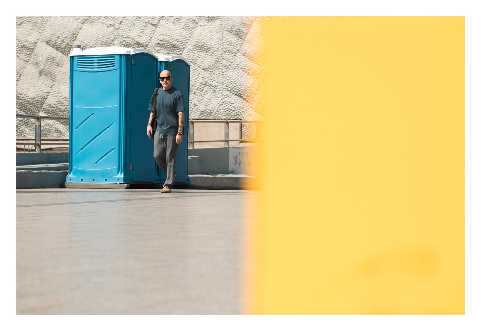 fotografo-callejear-persona-gafas-sol-calvo-cabina-baños-azul-amarillo.jpg